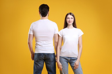 Photo of Woman and man wearing blank white t-shirts on orange background. Mockup for design