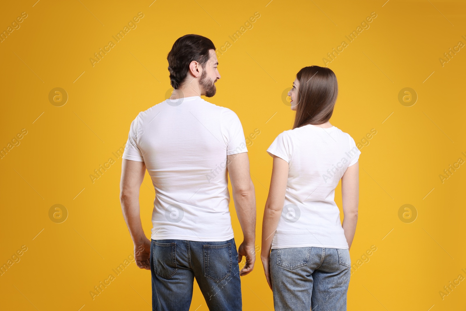 Photo of Woman and man wearing blank white t-shirts on orange background, back view. Mockup for design