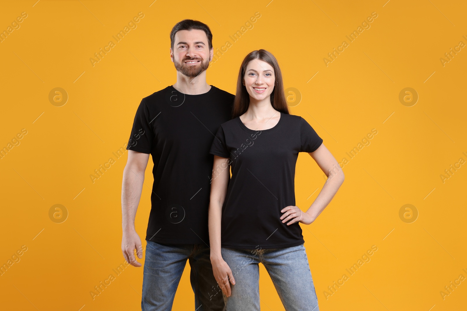 Photo of Woman and man wearing blank black t-shirts on orange background. Mockup for design