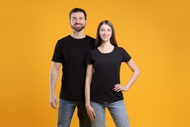 Photo of Woman and man wearing blank black t-shirts on orange background. Mockup for design