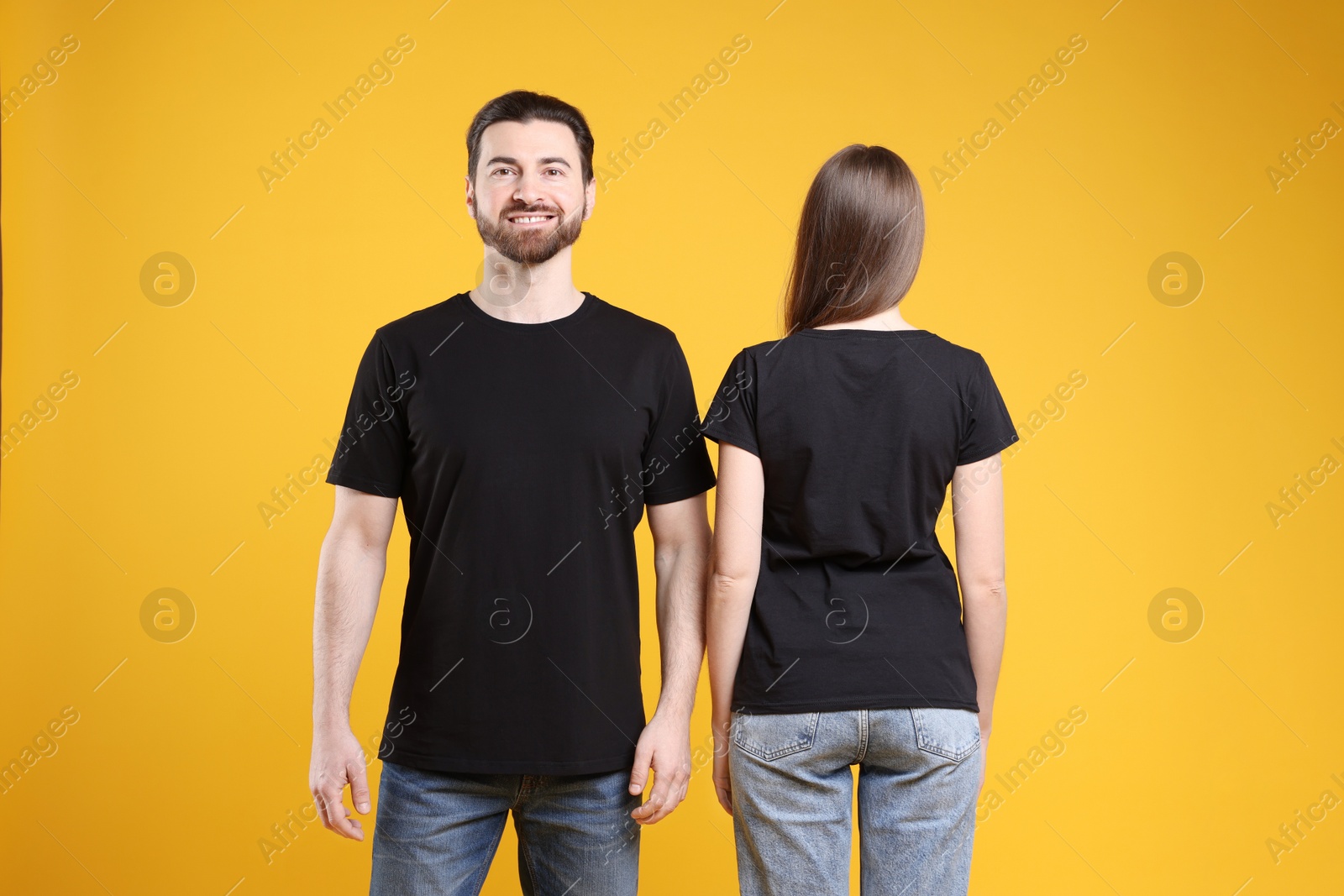 Photo of Woman and man wearing blank black t-shirts on orange background. Mockup for design