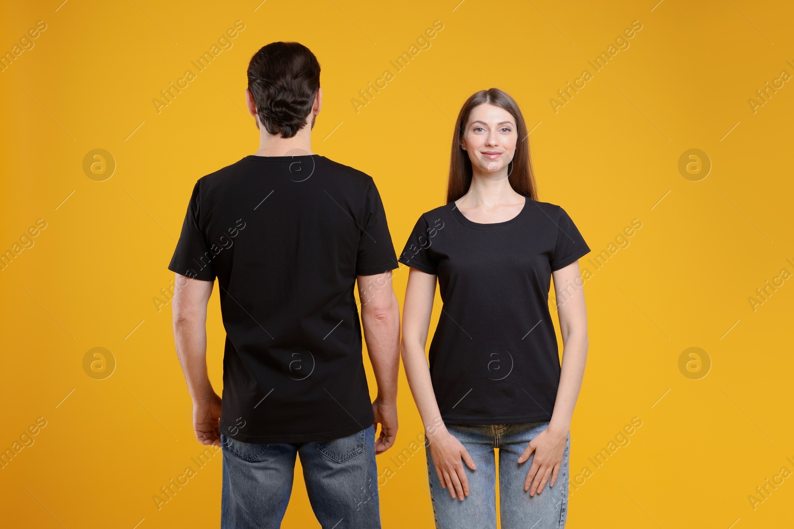 Photo of Woman and man wearing blank black t-shirts on orange background. Mockup for design