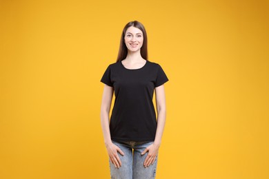 Photo of Woman wearing blank black t-shirt on orange background. Mockup for design