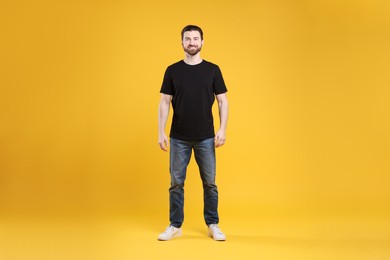 Photo of Man wearing blank black t-shirt on orange background. Mockup for design