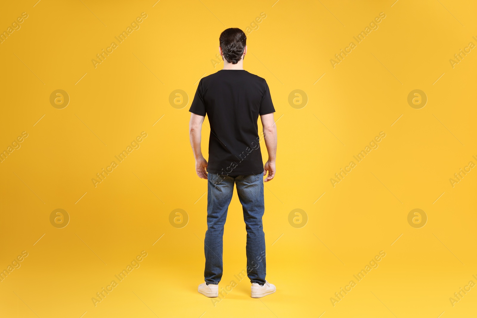 Photo of Man wearing blank black t-shirt on orange background, back view. Mockup for design