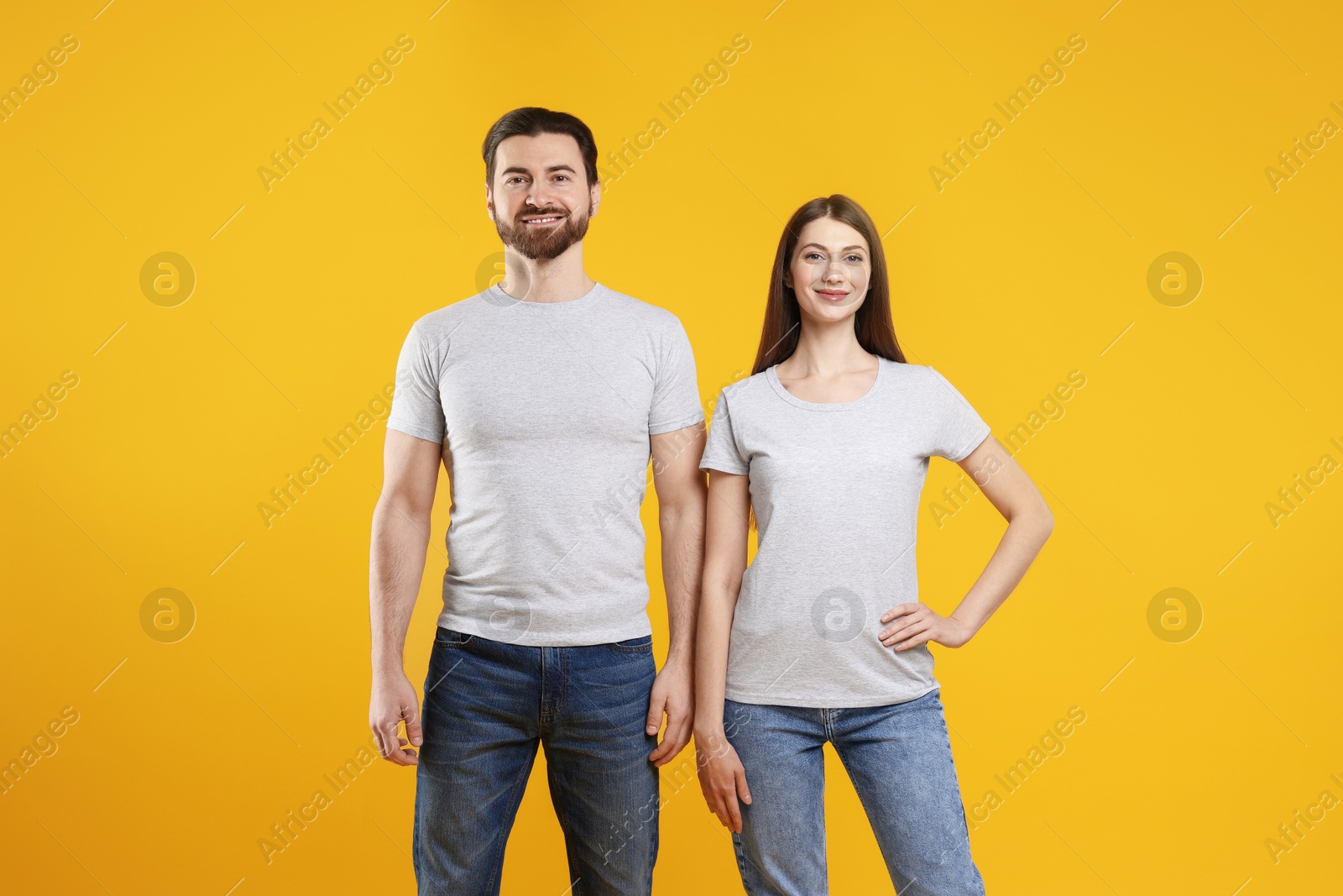 Photo of Woman and man wearing blank white t-shirts on orange background. Mockup for design