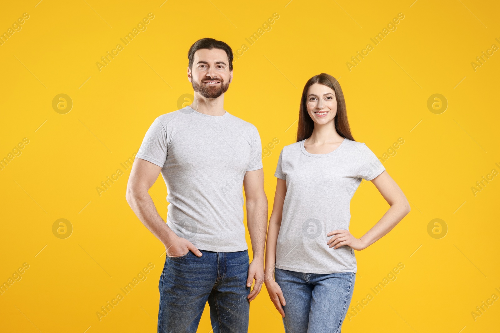 Photo of Woman and man wearing blank white t-shirts on orange background. Mockup for design