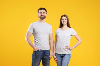 Photo of Woman and man wearing blank white t-shirts on orange background. Mockup for design