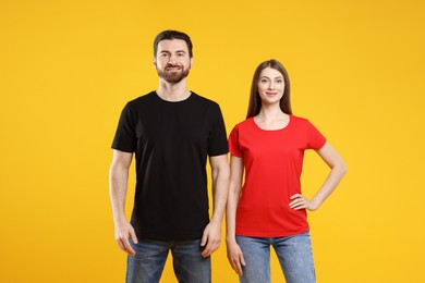 Photo of Woman and man wearing blank t-shirts on orange background. Mockup for design