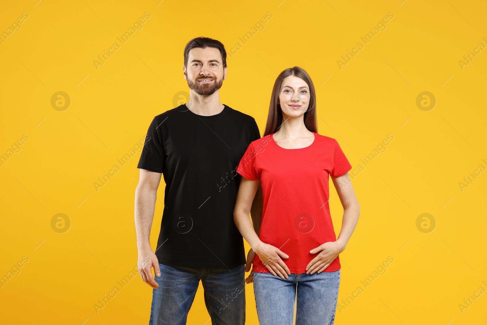 Photo of Woman and man wearing blank t-shirts on orange background. Mockup for design