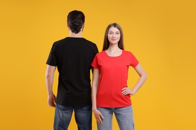 Photo of Woman and man wearing blank t-shirts on orange background. Mockup for design