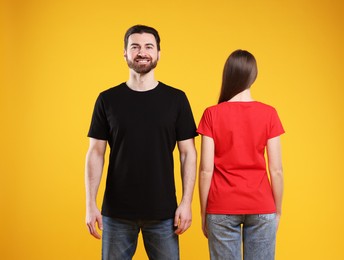 Photo of Woman and man wearing blank t-shirts on orange background. Mockup for design