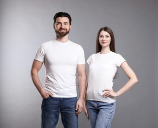 Photo of Woman and man wearing blank white t-shirts on light grey background. Mockup for design