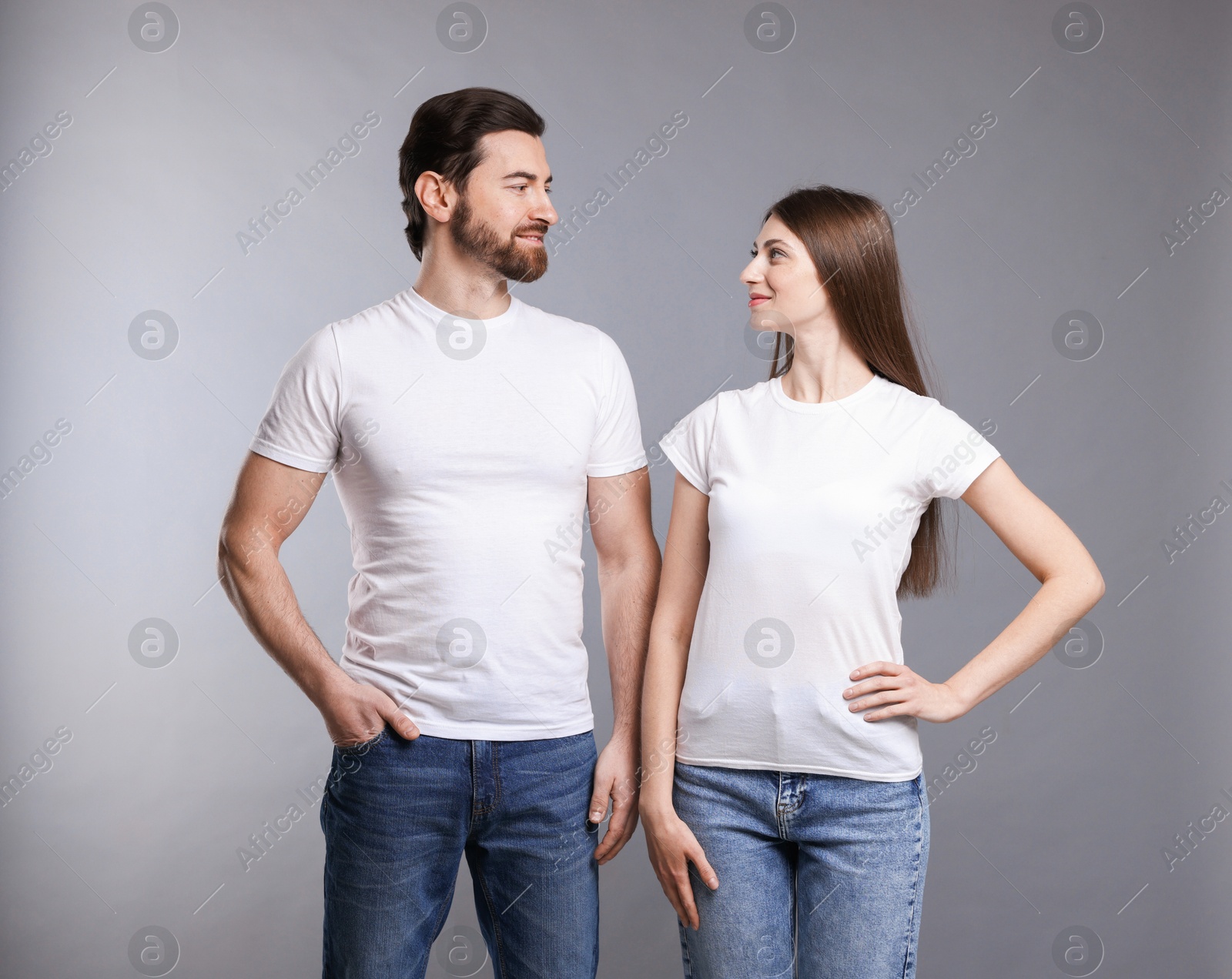 Photo of Woman and man wearing blank white t-shirts on light grey background. Mockup for design