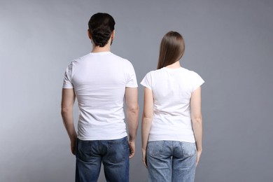 Photo of Woman and man wearing blank white t-shirts on light grey background, back view. Mockup for design