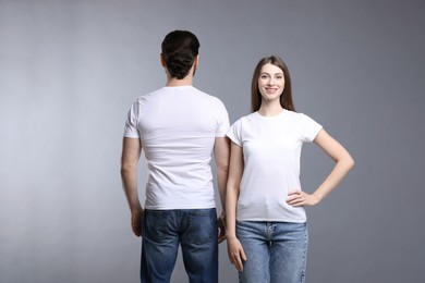 Photo of Woman and man wearing blank white t-shirts on light grey background. Mockup for design