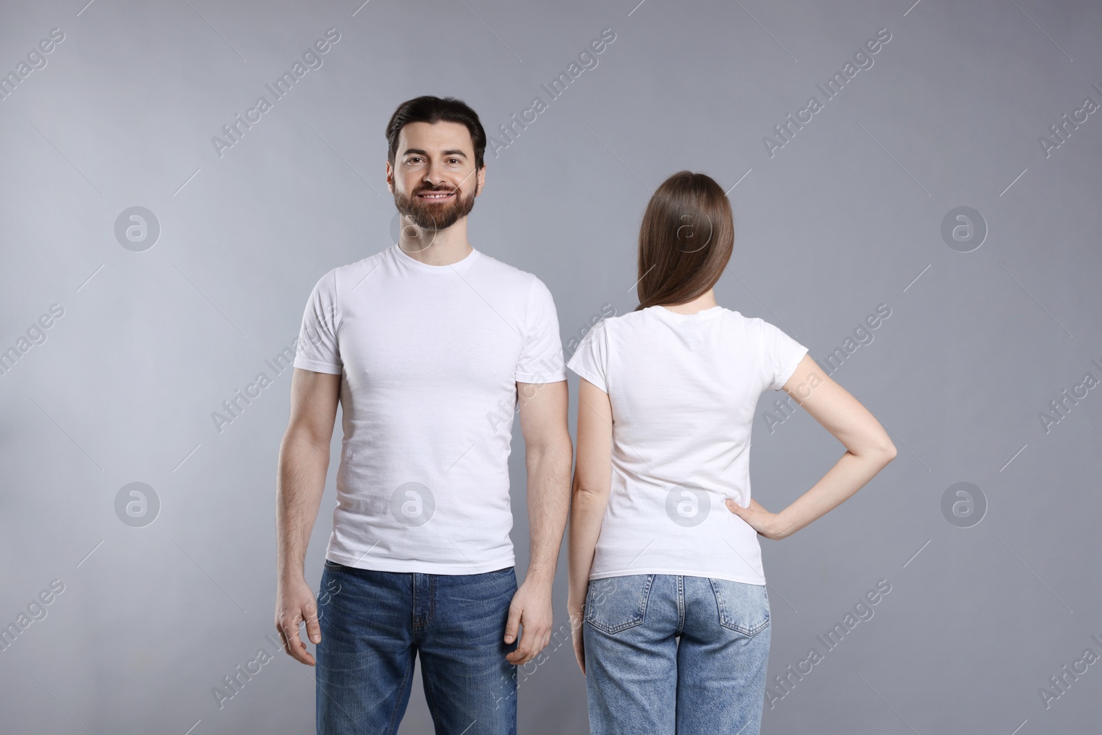 Photo of Woman and man wearing blank white t-shirts on light grey background. Mockup for design