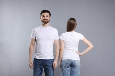 Photo of Woman and man wearing blank white t-shirts on light grey background. Mockup for design