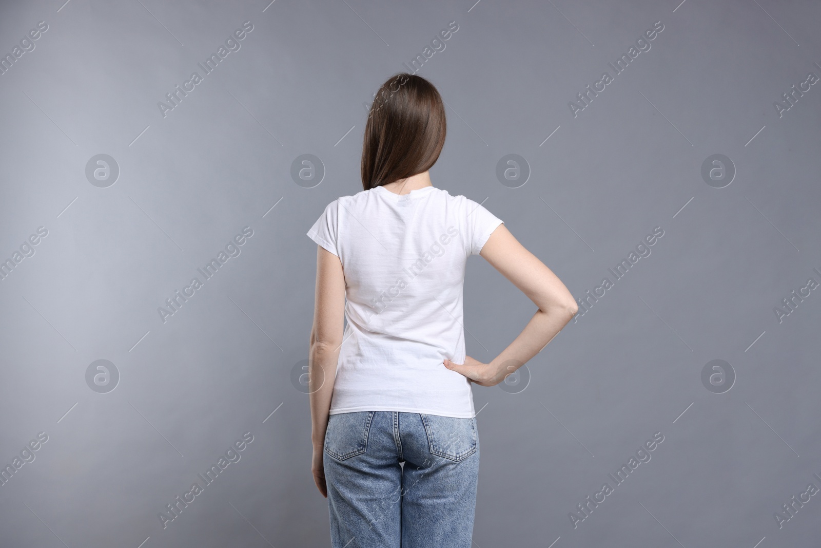 Photo of Woman wearing blank white t-shirt on light grey background, back view. Mockup for design