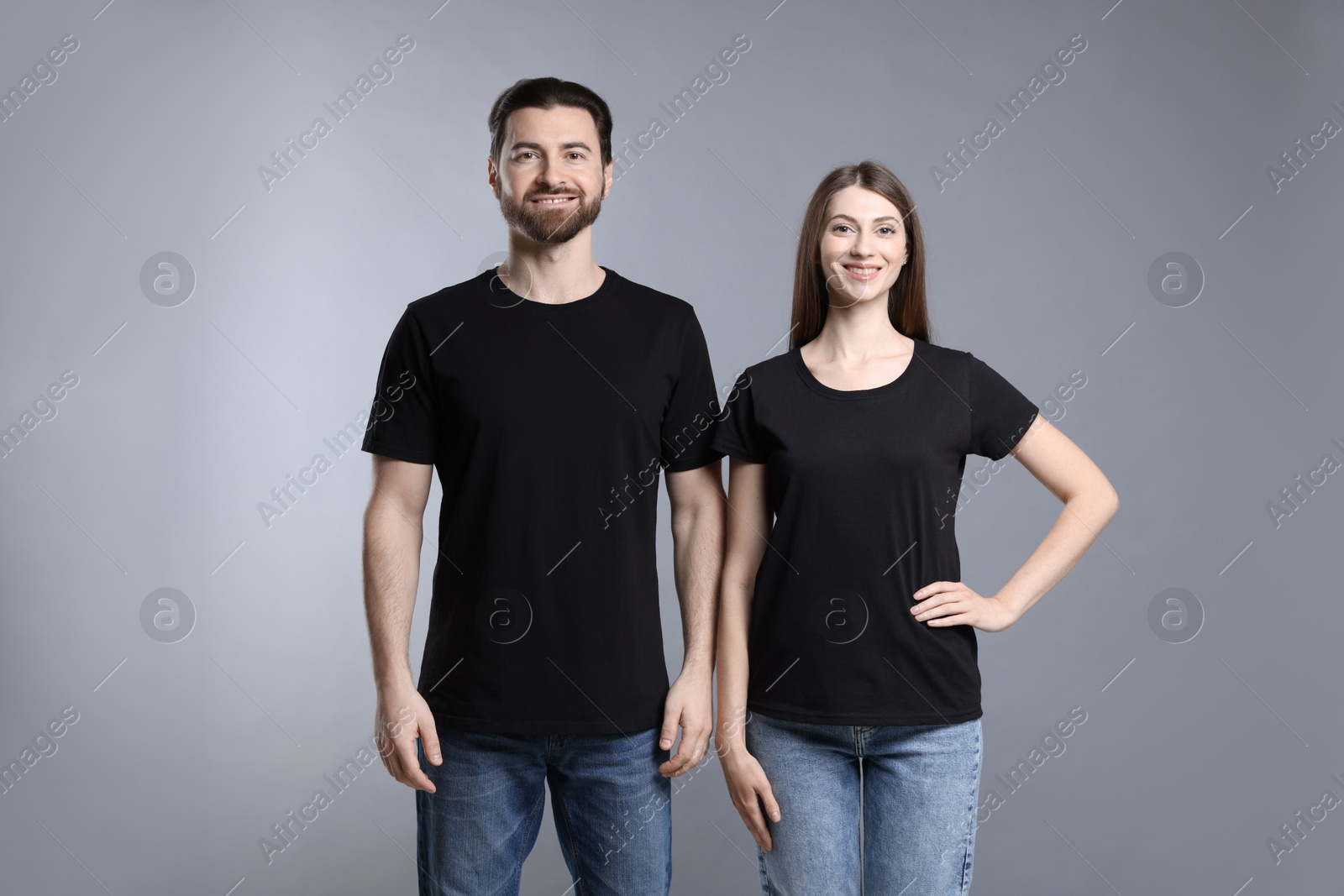 Photo of Woman and man wearing blank black t-shirts on light grey background. Mockup for design