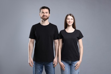 Woman and man wearing blank black t-shirts on light grey background. Mockup for design