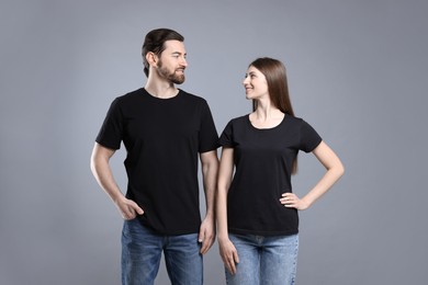 Photo of Woman and man wearing blank black t-shirts on light grey background. Mockup for design