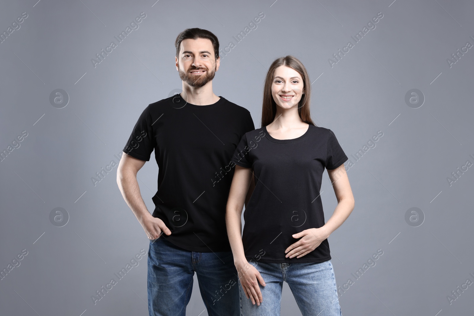 Photo of Woman and man wearing blank black t-shirts on light grey background. Mockup for design