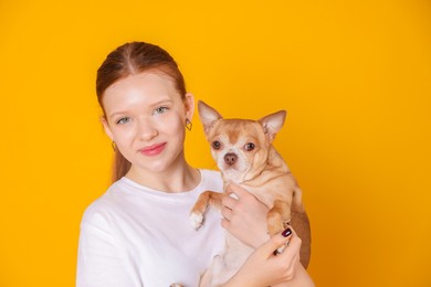 Photo of Teenage girl with her cute Chihuahua dog on yellow background, space for text