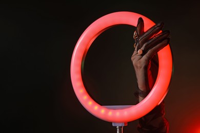 Photo of Woman wearing beautiful rings on dark red background, closeup. Using ring lamp