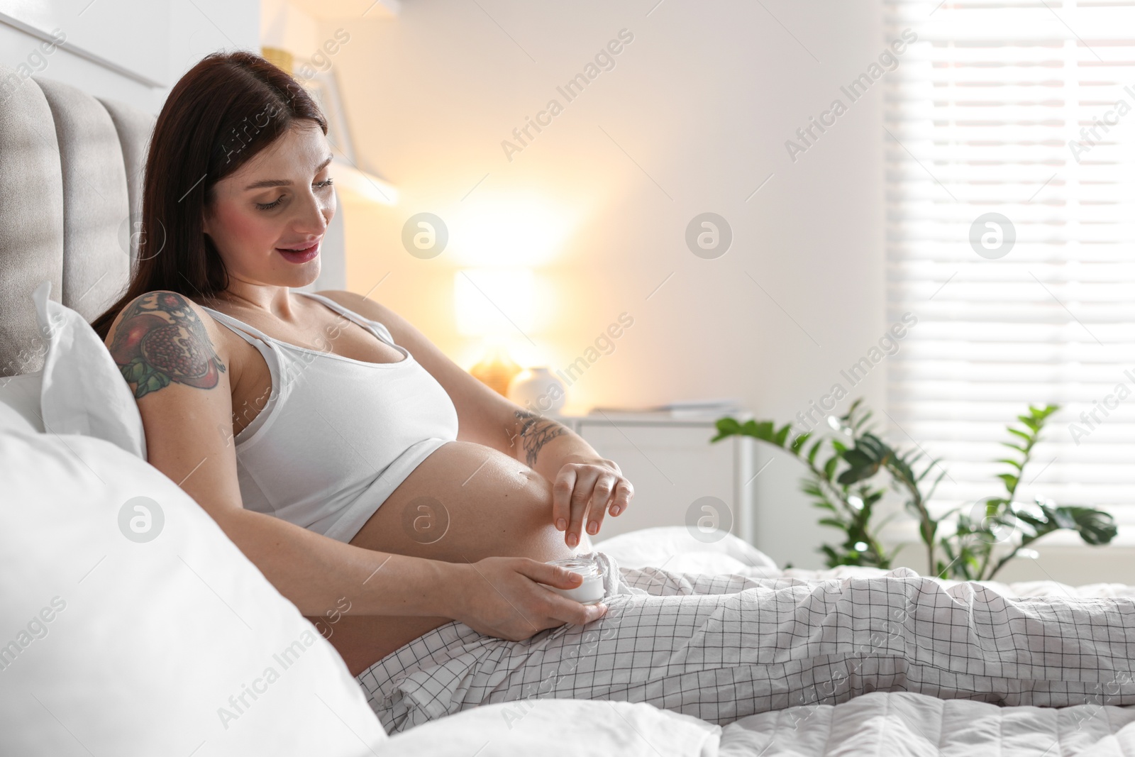 Photo of Pregnant woman with jar of cream on bed at home