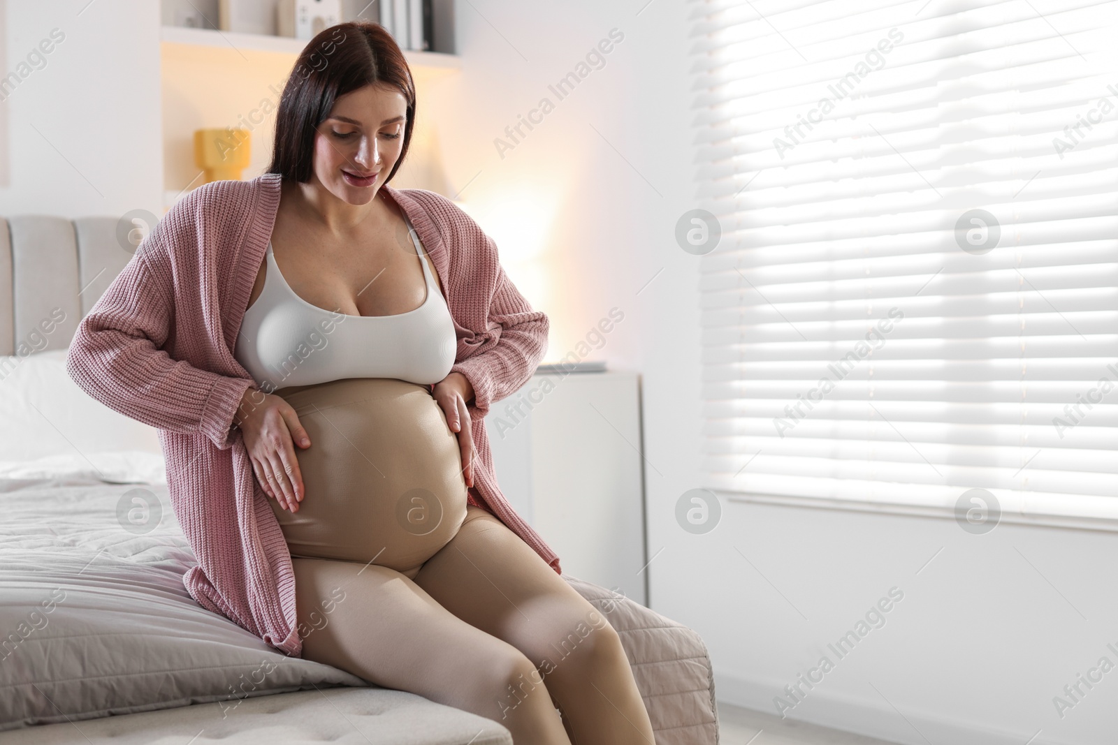 Photo of Beautiful pregnant woman with cute belly on bed at home, space for text