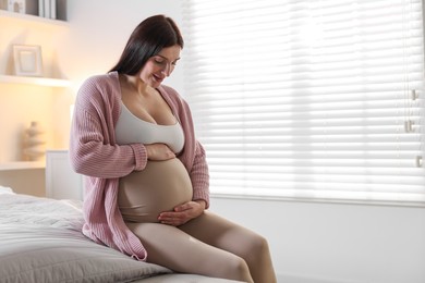 Photo of Beautiful pregnant woman with cute belly on bed at home, space for text