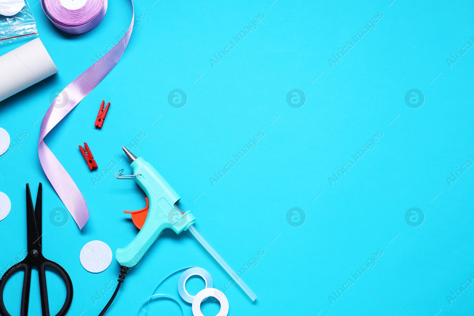 Photo of Hot glue gun and handicraft materials on light blue background, flat lay. Space for text