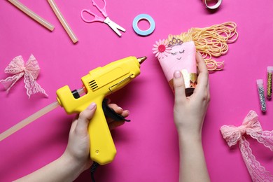 Photo of Woman with hot glue gun making craft on bright pink background, top view