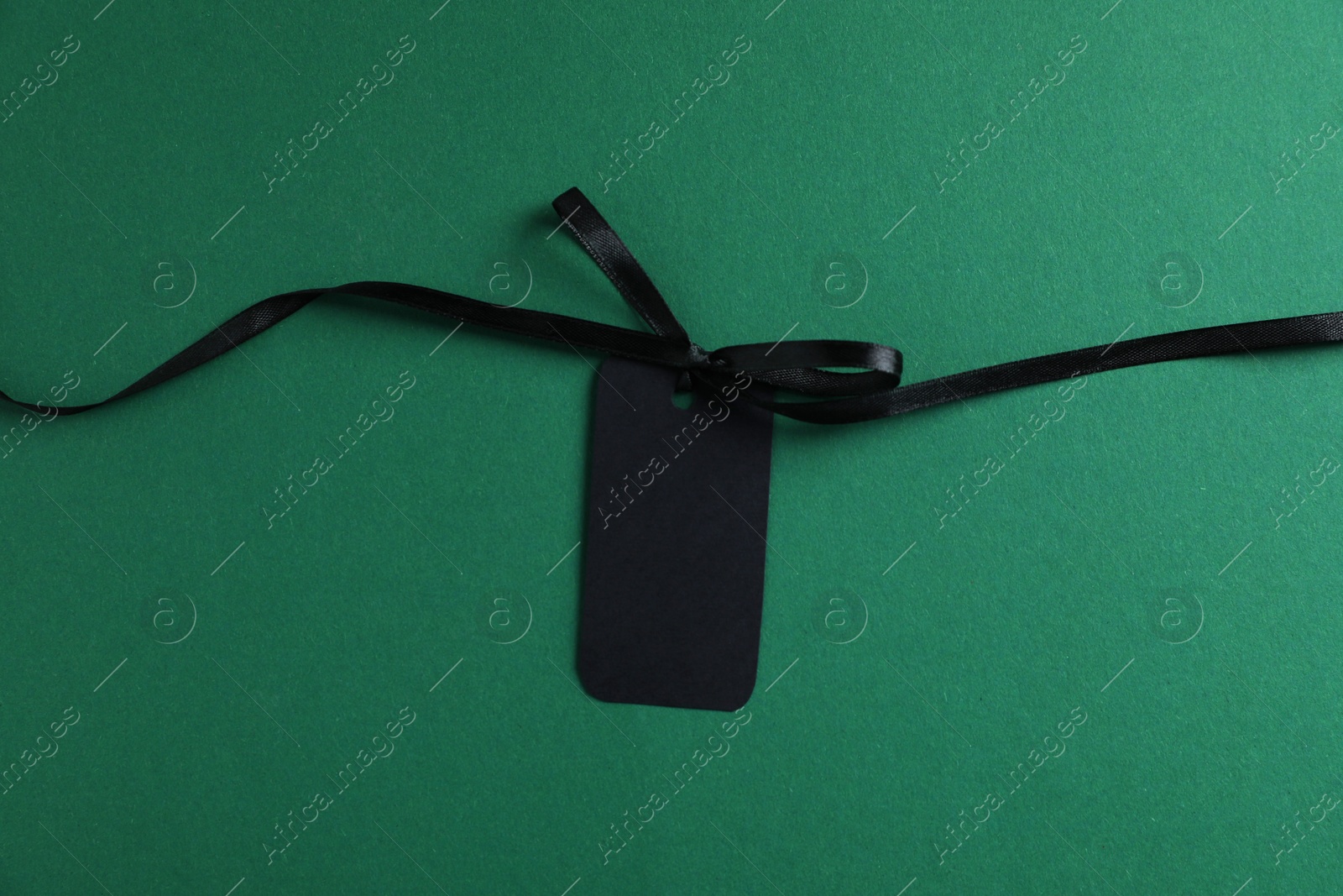 Blank tag with ribbon bow on green background, top view Photo of Blank tag with ribbon bow on green background, top view