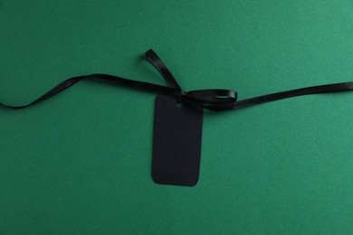 Photo of Blank tag with ribbon bow on green background, top view