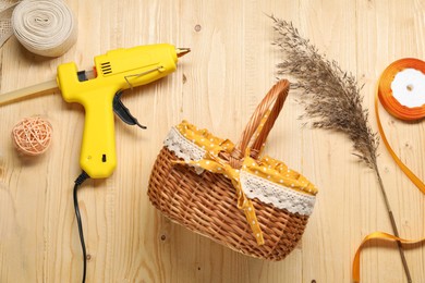 Photo of Hot glue gun and handicraft materials on wooden background, flat lay