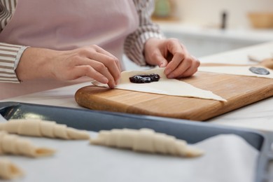 Photo of Woman rolling croissant with jam from fresh dough at table, closeup