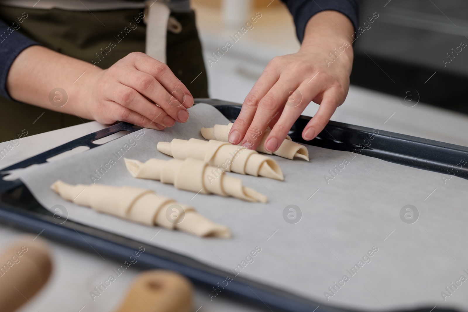 Woman putting raw croissants onto baking sheet at table indoors, closeup Photo of Woman putting raw croissants onto baking sheet at table indoors, closeup