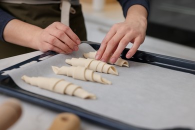 Photo of Woman putting raw croissants onto baking sheet at table indoors, closeup