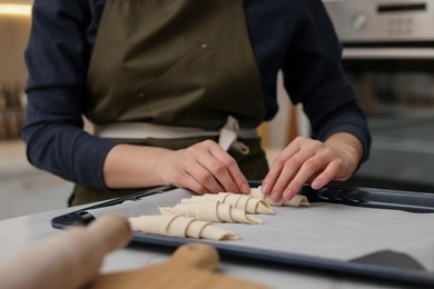 Photo of Woman putting raw croissants onto baking sheet at table indoors, closeup