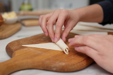 Photo of Woman rolling croissant from fresh dough at light table indoors, closeup