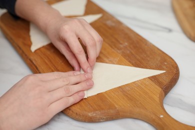 Photo of Woman rolling croissant from fresh dough at white marble table, closeup