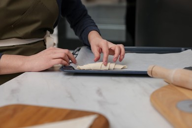 Photo of Woman putting raw croissant onto baking sheet at white marble table indoors, closeup