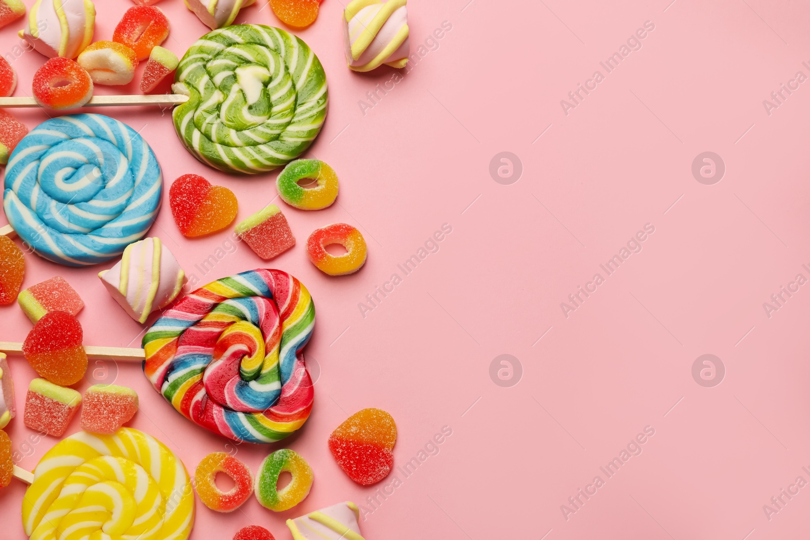 Photo of Many different tasty candies and marshmallows on pink background, flat lay. Space for text