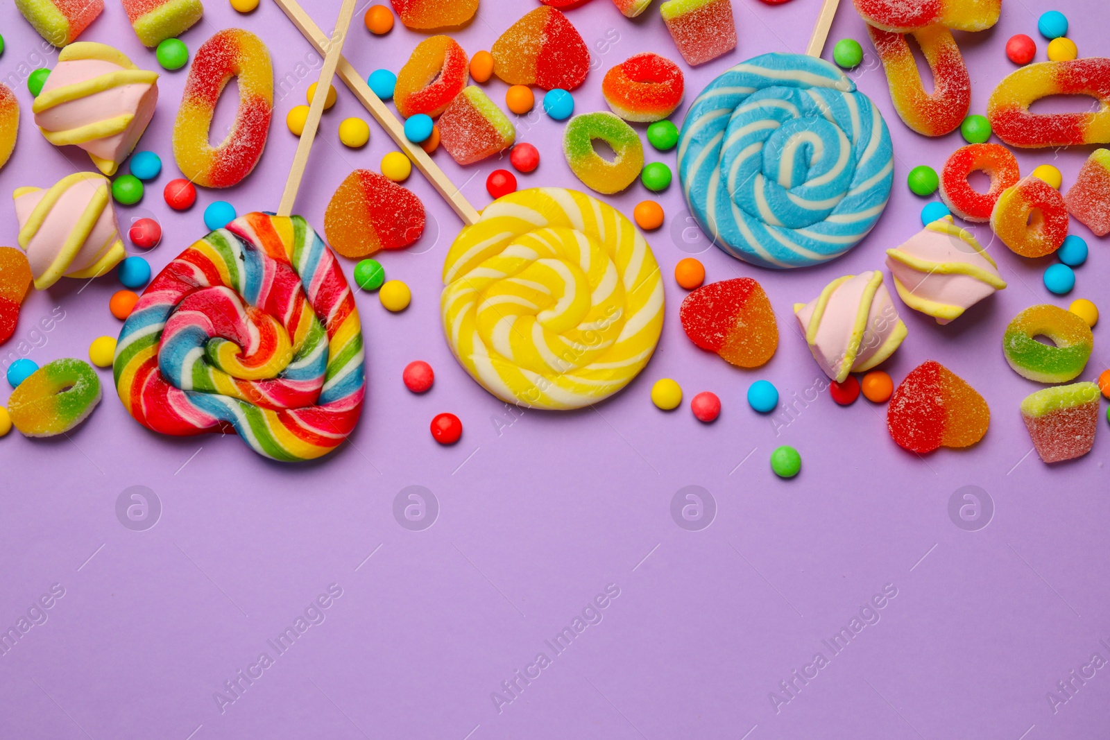 Photo of Many different tasty candies and marshmallows on violet background, flat lay. Space for text