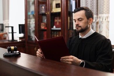 Photo of Judge with folder of documents at wooden table in courtroom