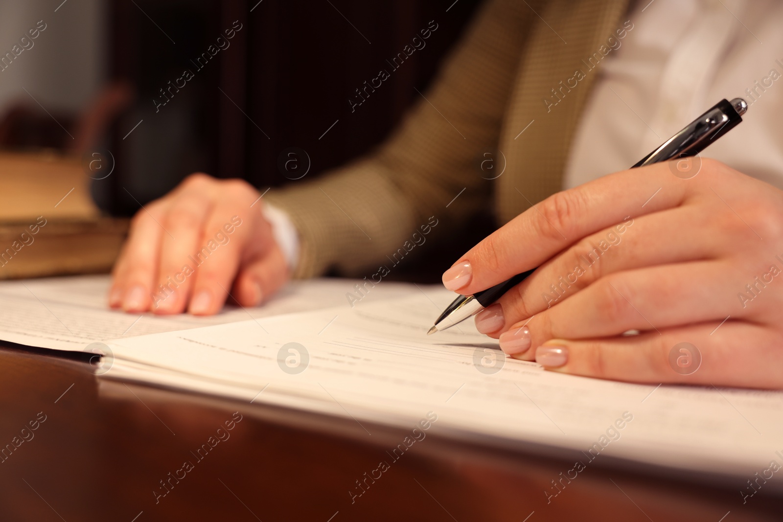 Photo of Notary signing document at table in office, closeup