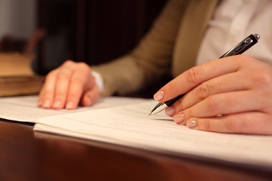 Photo of Notary signing document at table in office, closeup