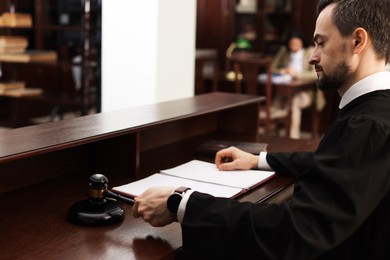 Photo of Judge striking gavel at wooden table in courtroom, selective focus